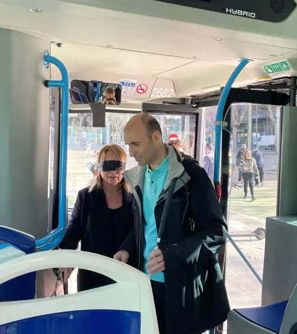 Una persona invidente y la regidora de Dependencia, con los ojos tapados accediendo a un autobús